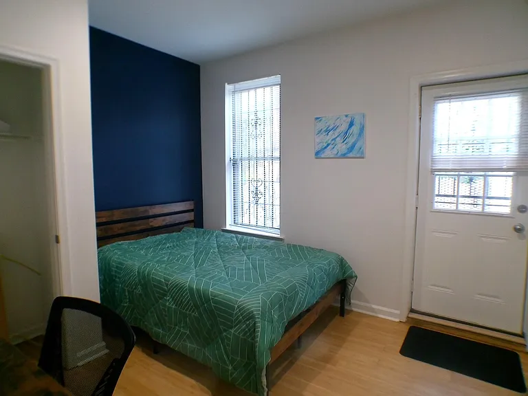 Furnished bedroom with a full bed, accent wall, and two windows plus a private exterior door for easy access.