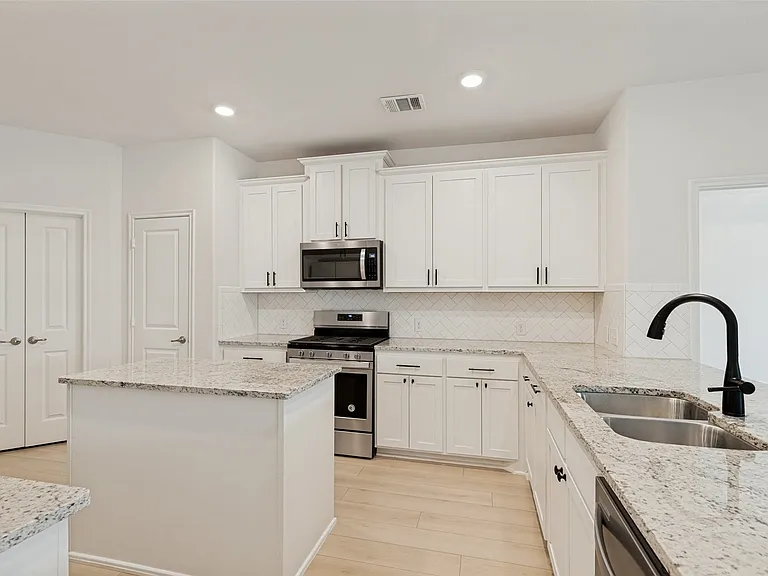 Kitchen featuring a central island, light-toned countertops, white cabinetry with dark hardware, stainless steel appliances, and wood-finish flooring