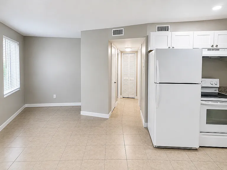 Bright and airy apartment kitchen showcasing modern white cabinetry, spacious tiled flooring, and natural light for a cozy living experience.
