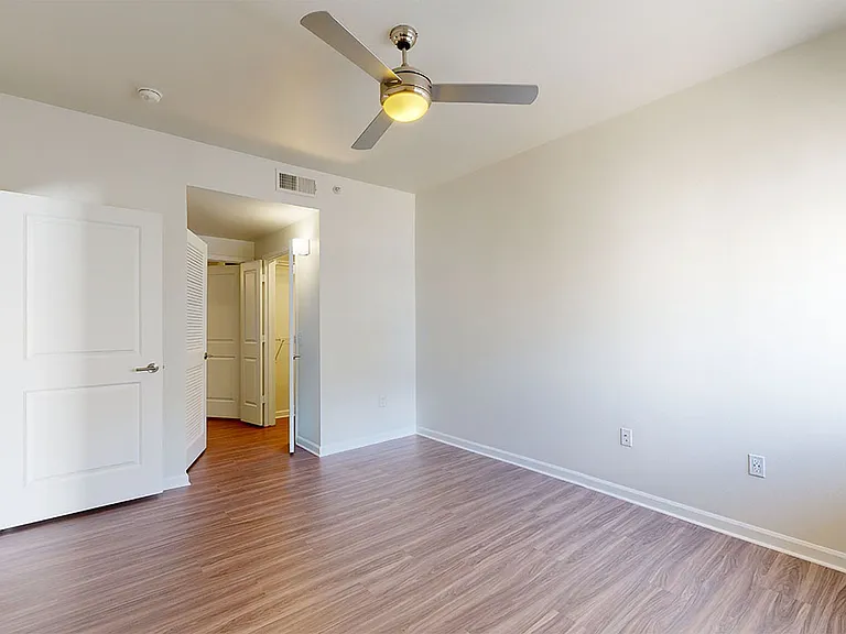 Spacious apartment bedroom with large closet, attached bathroom and wood style flooring.
