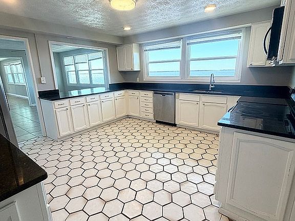 Bright and spacious kitchen with stylish hexagonal tile flooring, sleek black countertops, and ample white cabinetry, complemented by large sunlit windows.