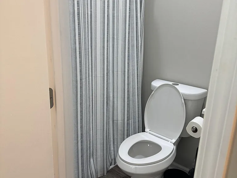 Full bathroom featuring a shower with curtain, updated flooring, and convenient toilet paper holder and waste bin.