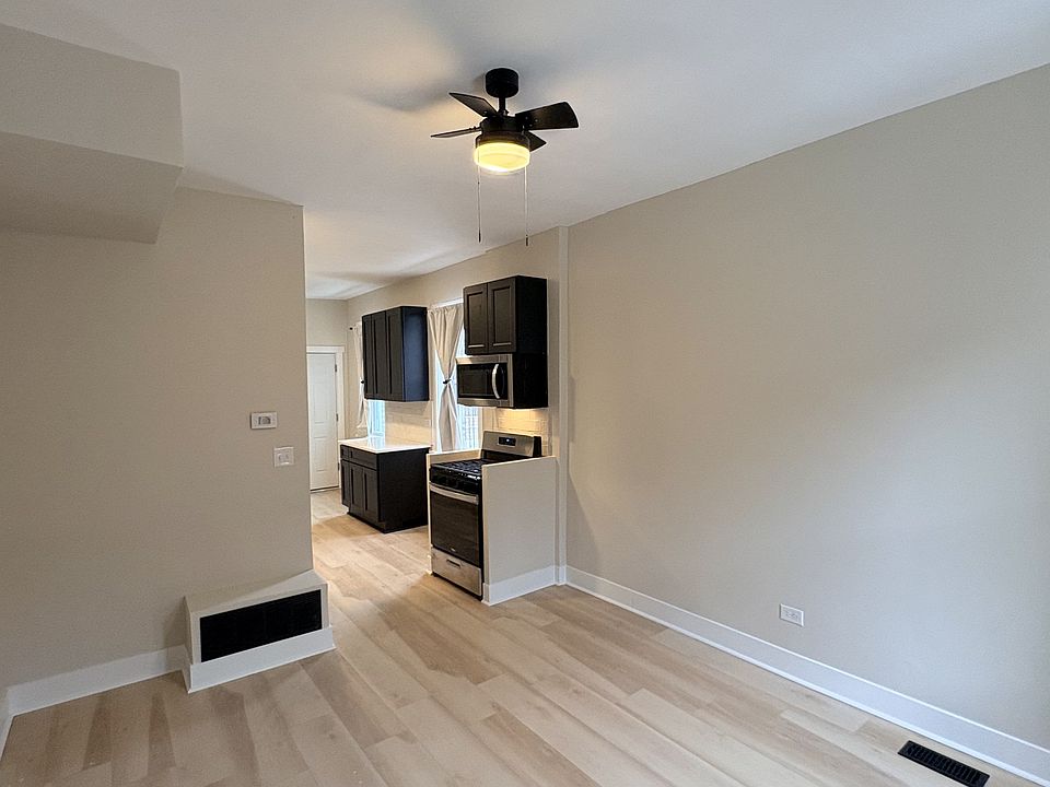 Spacious living area with ceiling fan, light wood flooring, and open flow into the modern kitchen