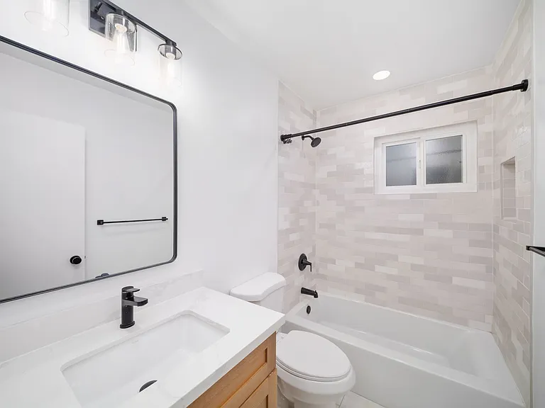 Modern, newly renovated bathroom complete with stylish tile, wooden vanity, and a quartz countertop.
