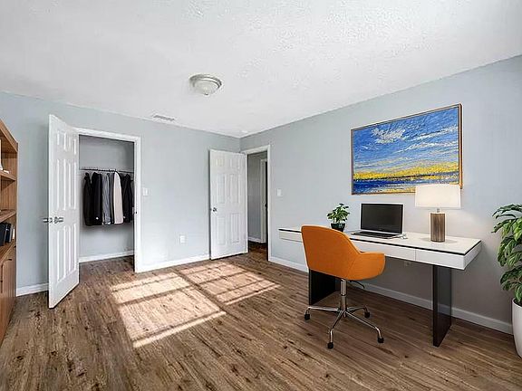 Bright and inviting home office with modern desk, orange chair, vibrant artwork, and wooden floors.