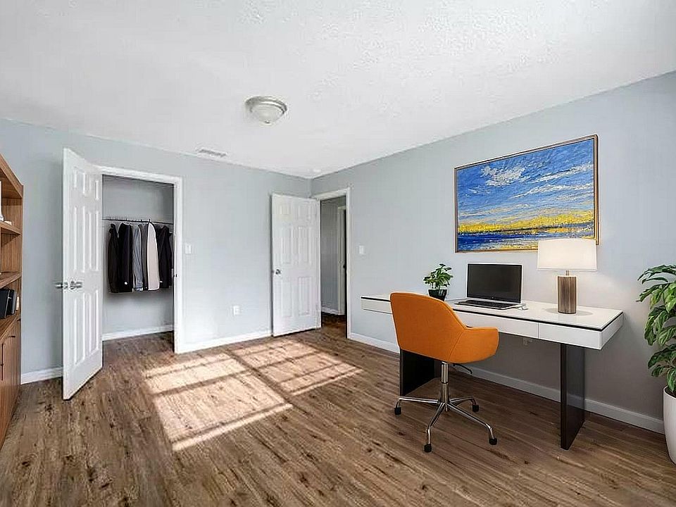 Bright and inviting home office with modern desk, orange chair, vibrant artwork, and wooden floors.