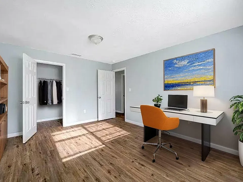 Bright and inviting home office with modern desk, orange chair, vibrant artwork, and wooden floors.