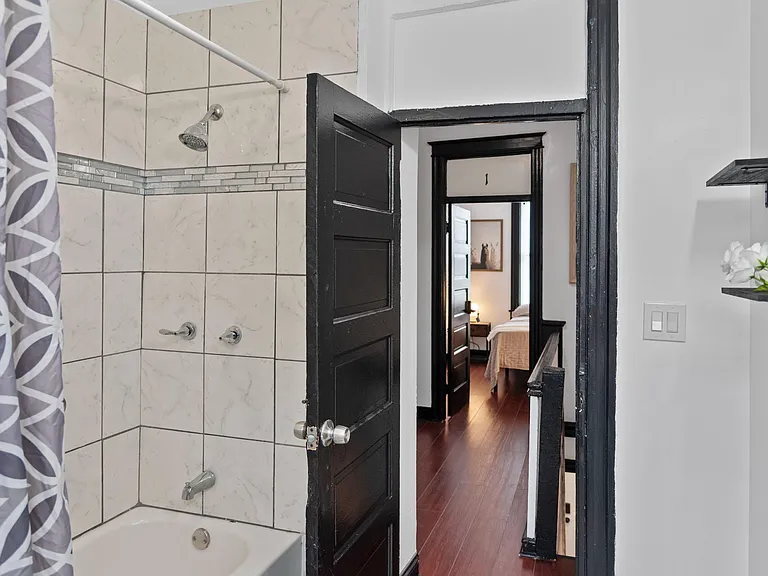 Full bath with tiled tub/shower surround, decorative accent band, and convenient shelving for everyday essentials.