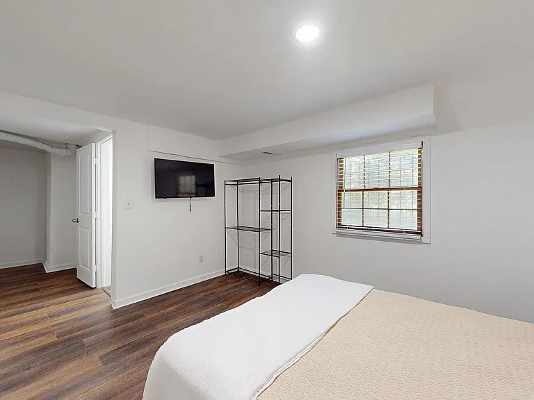 Bedroom with wood-look floors, a window with blinds, wall-mounted TV, and open shelving for extra storage.