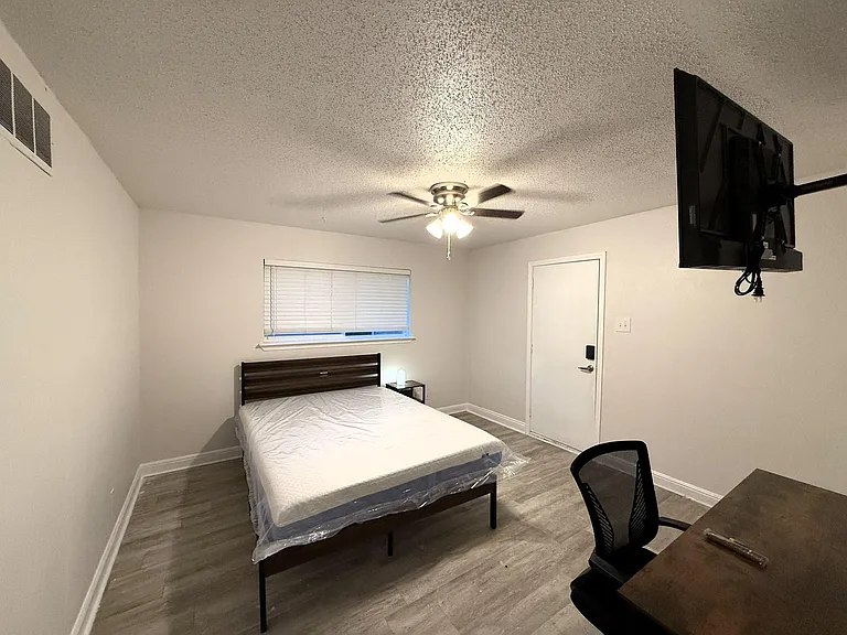 Private bedroom with a ceiling fan, window blinds, and space for a bed plus desk; includes a wall-mounted TV and easy-access