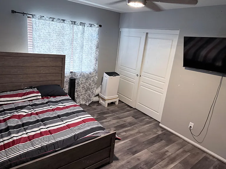 Furnished bedroom with wood-look flooring, a large closet with double doors, and a wall-mounted TV for easy living.