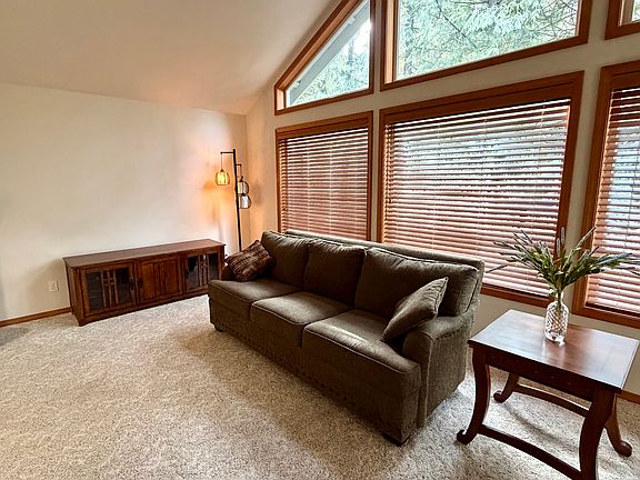Living room with high windows and wooden blinds. Two couches, lamps, side tables, and TV console are included if desired.