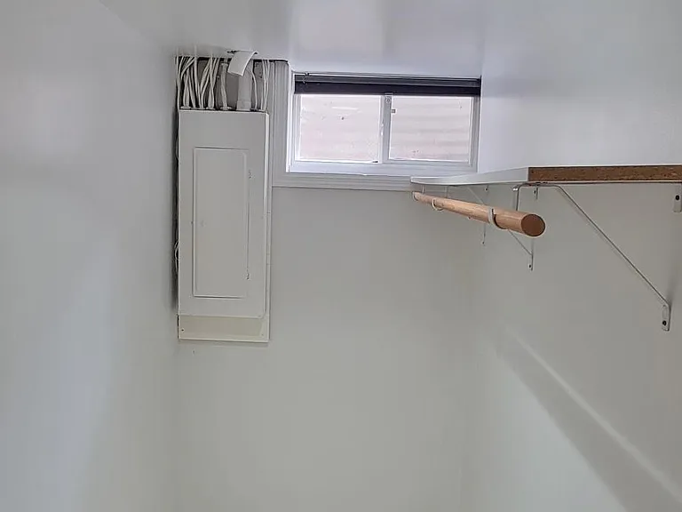 Storage room, electrical panel, bright light, shelf, and clothing rack.