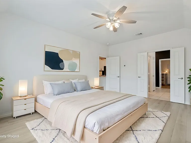 Spacious bedroom featuring light wood-finish flooring, a vaulted ceiling with a ceiling fan, and white walls