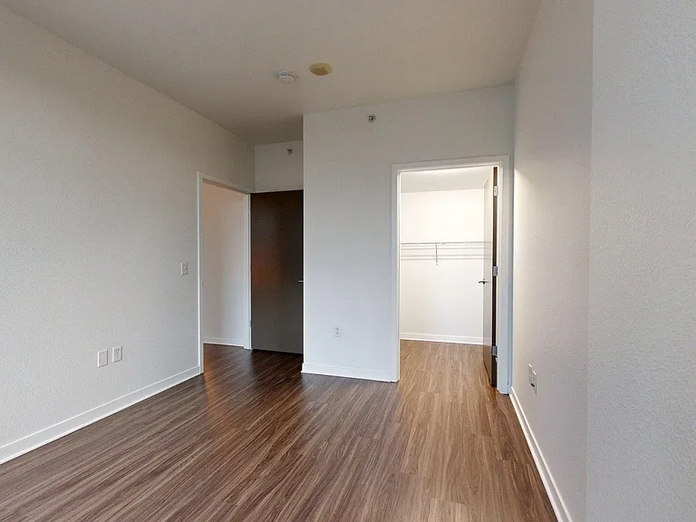 Spacious apartment bedroom with large closet and wood-style flooring.