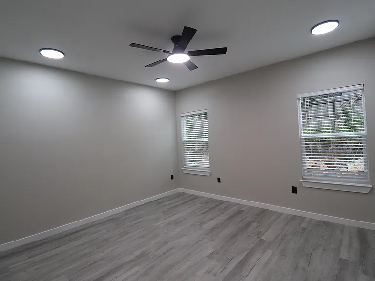 Bright primary bedroom with two windows, abundant natural light, modern flooring, and a stylish ceiling fan.
