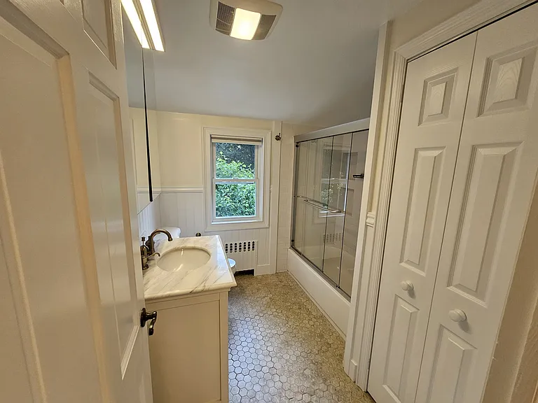 Private bathroom with heated tile floors, a glass-enclosed shower, vanity, and built-in storage.