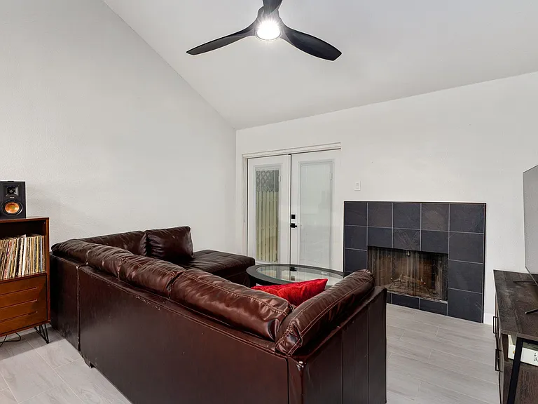 Living room with french doors, vaulted ceiling, ceiling fan, light wood-type flooring, and a tiled fireplace
