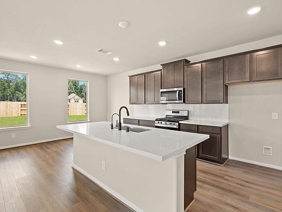 The kitchen features wood stained cabinetry with quartz countertops and a modern tile backsplash.