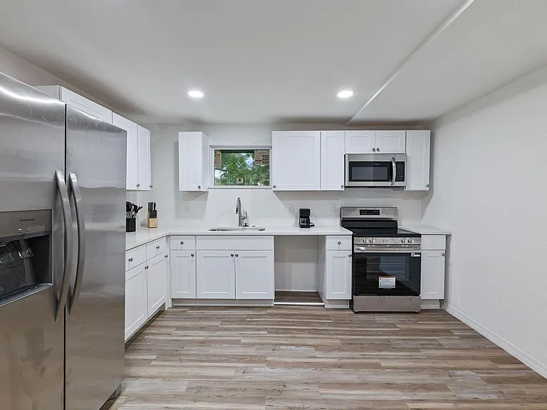 U-shaped kitchen with ample white cabinetry, generous counter space, and stainless steel appliances, plus a window over the s