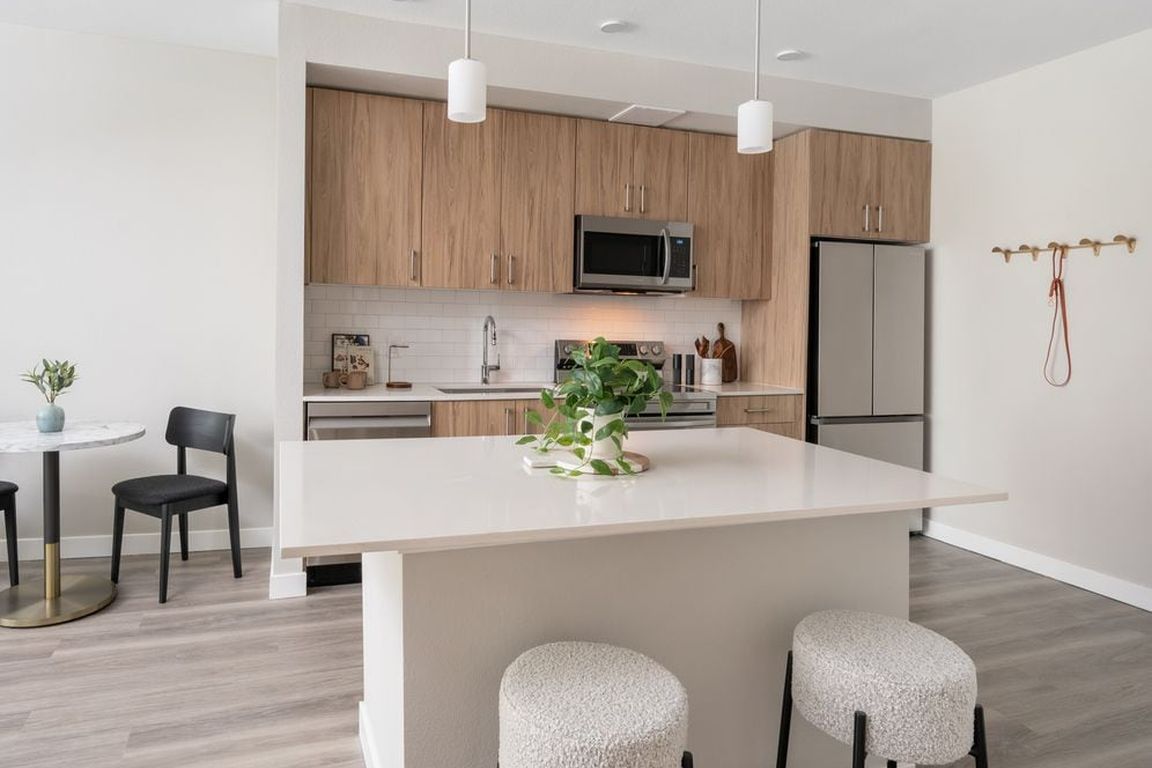 Finish Package II Kitchen with oak cabinetry, white quartz countertops, white tile backsplash, stainless steel appliances, pendant lighting, and hard-surface vinyl plank flooring
