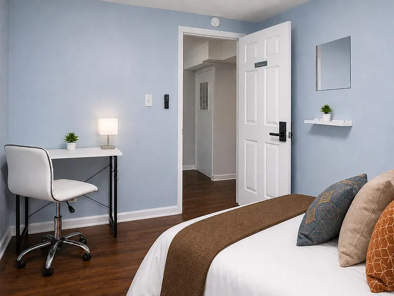 Furnished bedroom featuring a work desk and chair, wood-style flooring, and easy access to the hallway just outside.