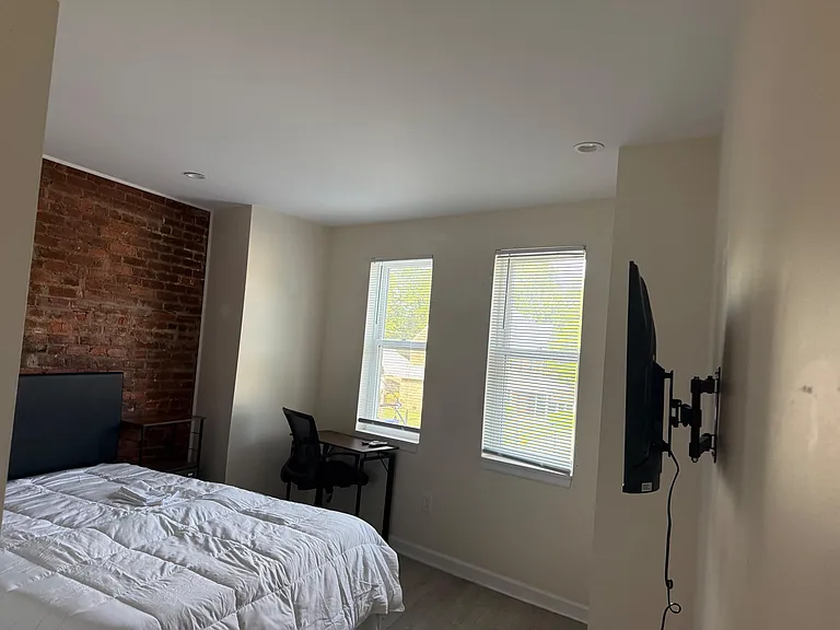 Bedroom with two windows and blinds, a dedicated desk/work area, and an exposed brick accent wall for added character.