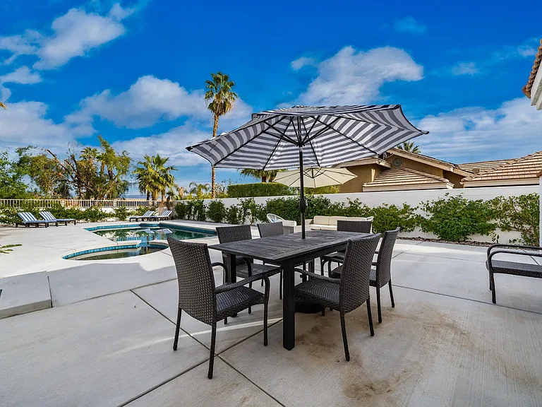 Dining area with umbrella by pool/spa.