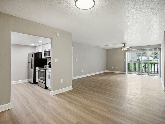 Bright and spacious open-plan living room with elegant wood flooring, modern kitchen appliances, and large sliding doors leading to a scenic balcony view.