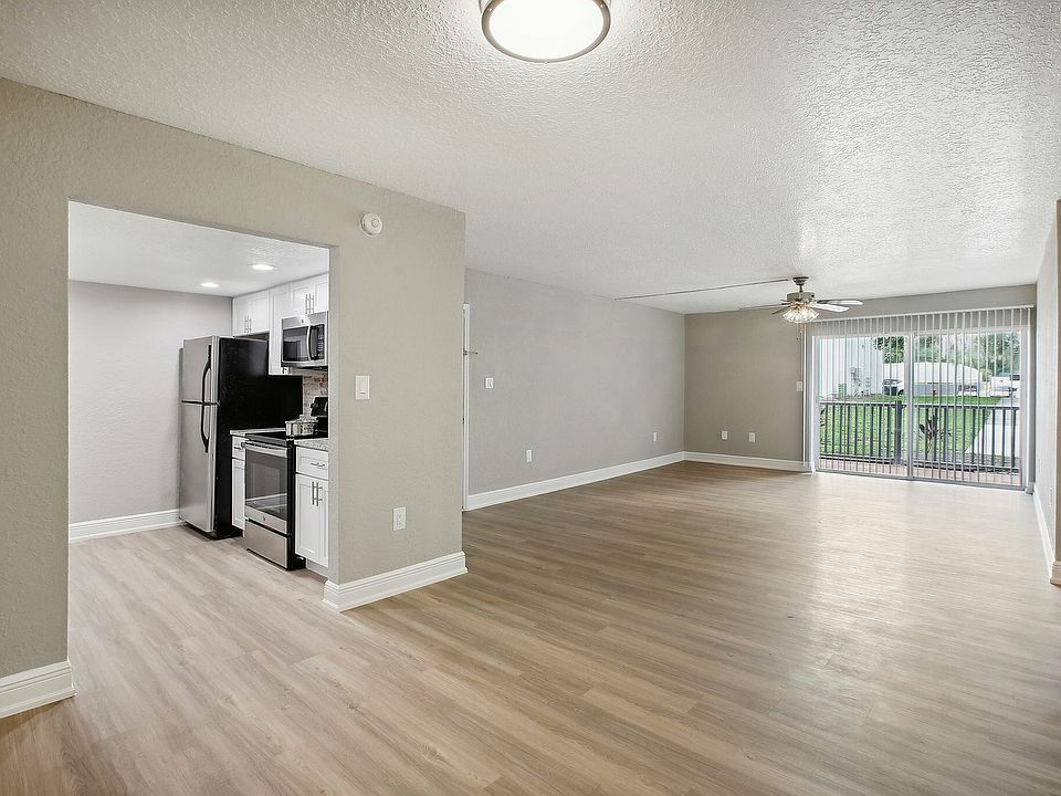 Bright and spacious open-plan living room with elegant wood flooring, modern kitchen appliances, and large sliding doors leading to a scenic balcony view.