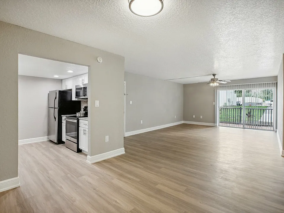 Bright and spacious open-plan living room with elegant wood flooring, modern kitchen appliances, and large sliding doors leading to a scenic balcony view.