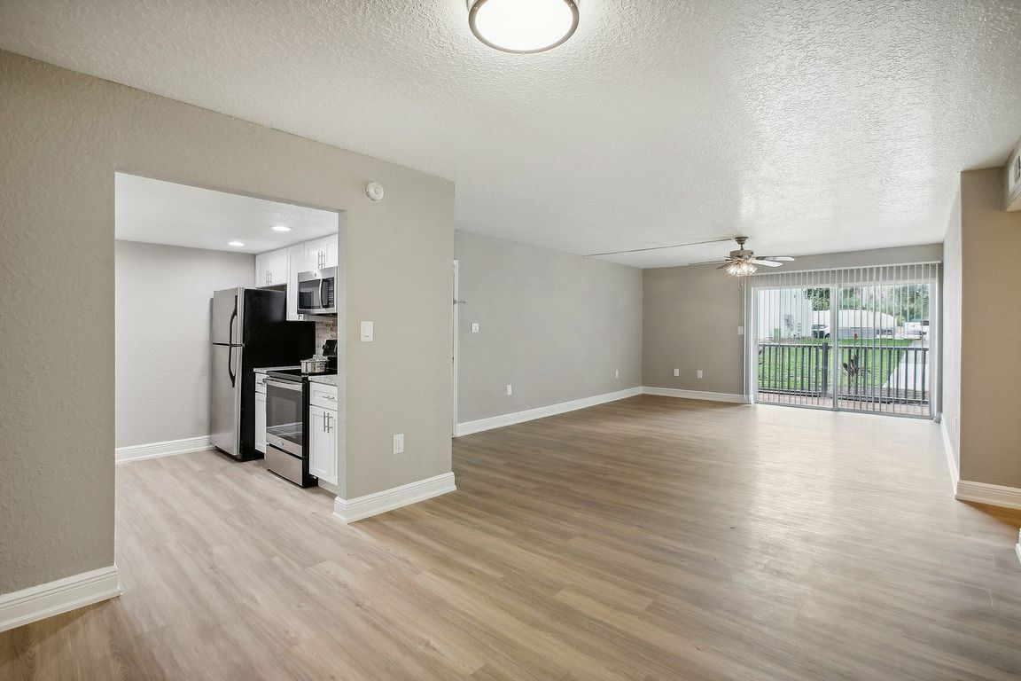 Bright and spacious open-plan living room with elegant wood flooring, modern kitchen appliances, and large sliding doors leading to a scenic balcony view.