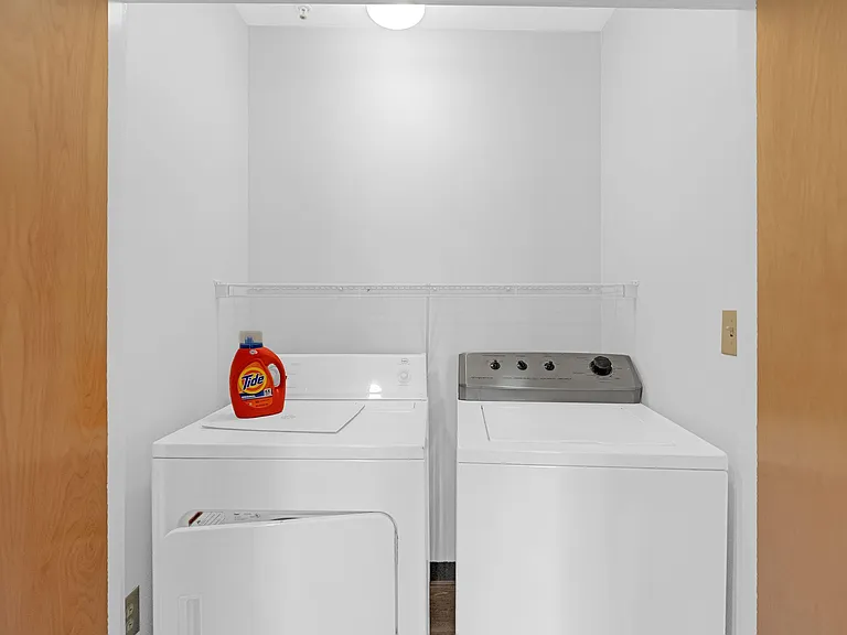 Dedicated laundry closet with side-by-side washer and dryer and a wire shelf for convenient storage.