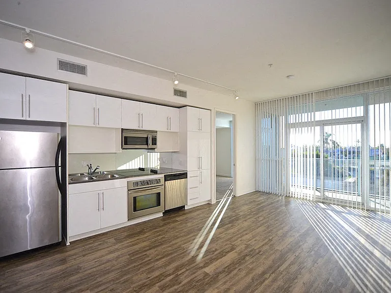 Large living room with hardwood floors, sliding doors to balcony and open kitchen at 12th Street Lofts in National City, California..