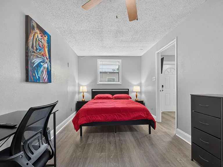 Furnished bedroom with full bed, nightstands, dresser, and dedicated desk space, plus a window and ceiling fan.