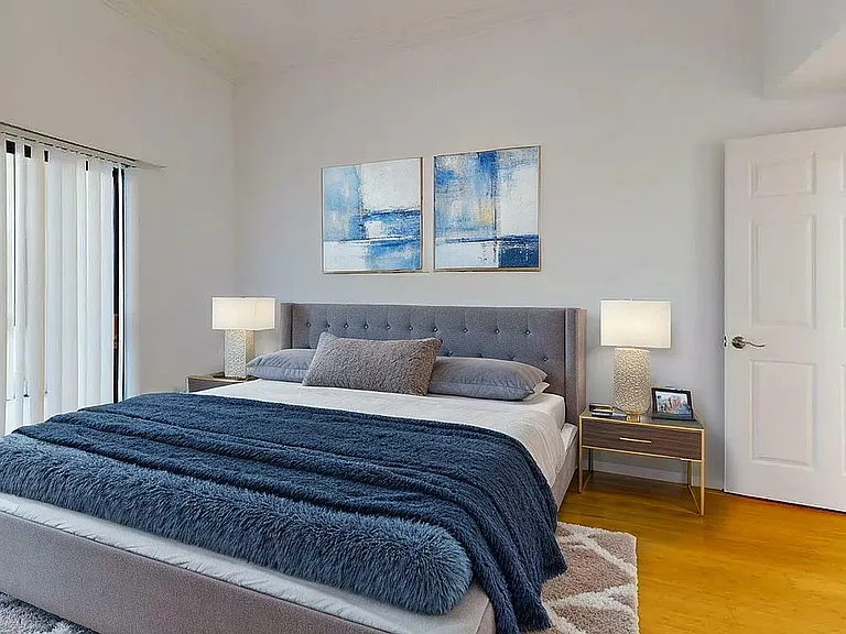 Elegant bedroom featuring a luxurious bed with plush bedding, modern bedside tables with lamps, chic abstract art, and natural light from large windows.
