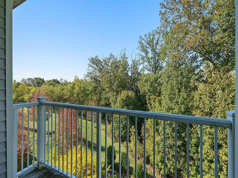 Serene apartment balcony view overlooking lush green trees and a clear blue sky, perfect for relaxation.