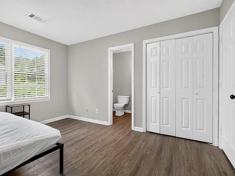 Bedroom with wood-look flooring, large window with blinds, and wide closet; convenient access to an en-suite bath.