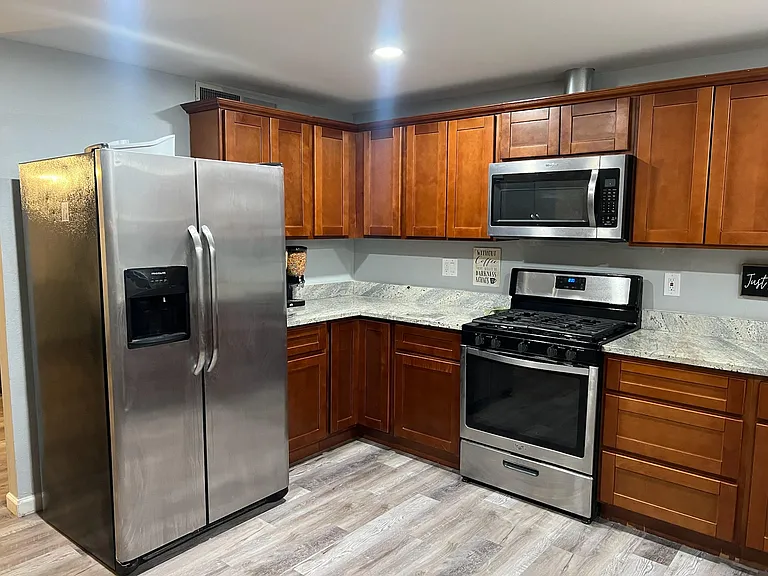 L-shaped kitchen with ample wood cabinetry, stone-look counters, and stainless steel fridge, range, and microwave.