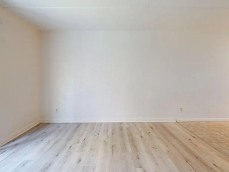 Bright and spacious room with stylish wood and tile flooring separated by a seamless transition, enhanced by natural light from vertical blinds.