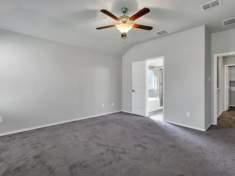 Carpeted room featuring a vaulted ceiling with a ceiling fan light fixture, light gray walls, white baseboards, and two interior doorways