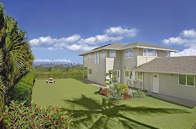 Big fenced in back yard with palm tree, flowers and well manicured lawn.
