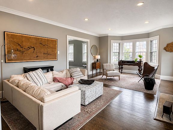 Spacious living room with a comfortable seating area, hardwood floors, and a sunlit bay window ideal for relaxing or working.