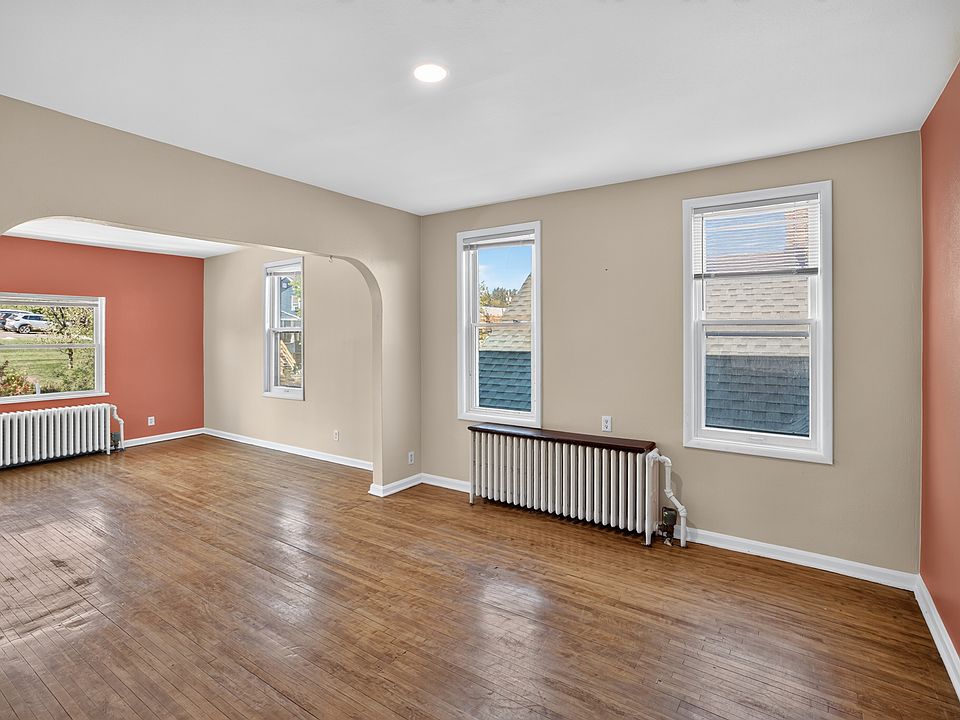 Another perspective of the expansive living and dining space, highlighting classic hardwood floors, an elegant architectural archway, radiator heat, and multi-directional natural light throughout.