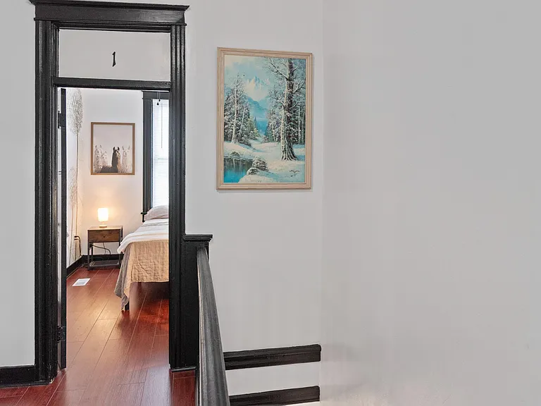 Private bedroom with hardwood floors, a nightstand, and space for a full bed, accessed from the hallway.