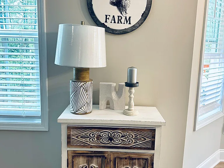 Sunlit corner with two large windows, neutral walls, and a decorative console cabinet ideal for added storage.