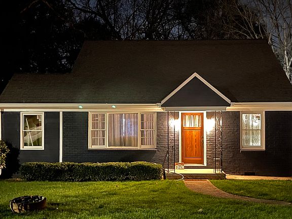 Beautifully lit at night, this navy blue home features a glowing wood front door, crisp white trim, and cozy curb appeal. Framed by hedges and a curved walkway, it offers a warm welcome on a quiet, EAV street_perfect for comfortable living.