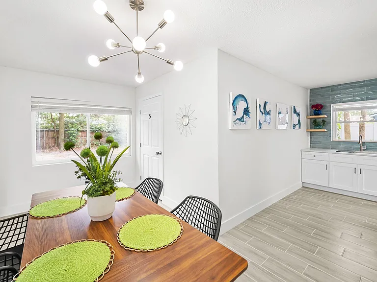Open kitchen with ample cabinetry, tile backsplash, and adjacent dining area with large window and updated lighting.