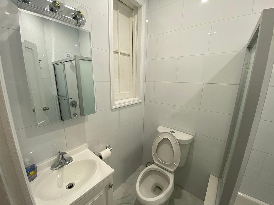 Bright renovated bathroom - Mirror medicine cabinet with vanity lights, sink with cabinet space underneath, new toilet, brand new shower/tub, and newly tiled walls and floors.