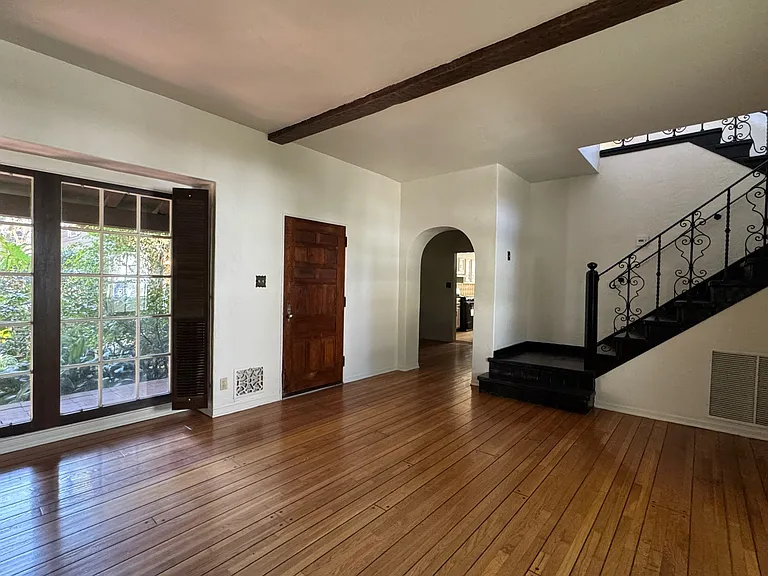 Living/entry - open layout with arched doorway to dining/kitchen, Spanish wooden front door, wood-paneled window, and staircase to the 2nd floor.
